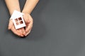 Top view on child hands holding white paper house on gray background. Family home and real estate concept. Royalty Free Stock Photo