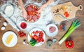 Top view of child making pizza with pizza ingredients, tomatoes, salami and mushrooms