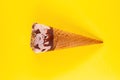 Chocolate flavor ice cream cone starts melting on yellow background