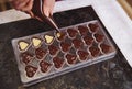 Top view of chocolatier squeezing filling of creamy liquid preparing luxury handmade chocolate pralines at home kitchen