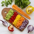 Top view, chopped fresh vegetables carrot, celery, onion, colored peppers arranged on cutting board on a white wooden surface. Royalty Free Stock Photo