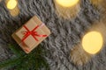 Top view of a Christmas gift box with a red ribbon, blur lights, and pine branches on a cozy carpet Royalty Free Stock Photo