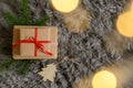 Top view of a Christmas gift box with a red ribbon, blur lights, and pine branches on a cozy carpet Royalty Free Stock Photo