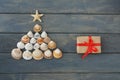 Top view of christmas tree shape made from sea shells and wrapped giftbox with red ribbon on wooden background, Royalty Free Stock Photo