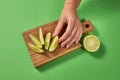 A woman`s hand takes a slice of organic fresh green lime on a wooden cutting board. Slices of lime on a board on a green Royalty Free Stock Photo