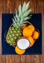 top view of citrus fruits as pineapple coconut tangerine orange in basket on jeans cloth and wooden background