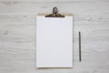 Top view, clipboard with blank sheet of paper and pencil over white wooden background. Flat lay, overhead