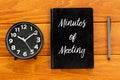 Top view of clock,pen and notebook written with Minutes of Meeting on wooden background. Business and finance concept.