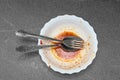 Top view close-up fork and spoon lie in white dirty plate, gray background, copy space. Dirty dishes after dinner Royalty Free Stock Photo