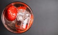 Top view close up on isolated cocktail glass with red strawberries, sparkling tonic water and ice cubes focus on ice cube right