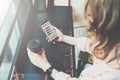 Top view. Close-up of smartphone and cup of coffee in hands of hipster girl sitting in cafe at black table.