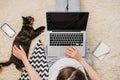 Top view close up of young girl sitting on floor using laptop computer typing studying working online, next lying small dark cat Royalty Free Stock Photo