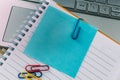 Top view closeup of a blue sticky note inside of a notebook, secured with a paper clip and a laptop Royalty Free Stock Photo
