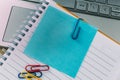 Top view closeup of a blue sticky note inside of a notebook, secured with a paper clip and a laptop