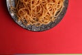 Top view closeup of delicious spaghetti pasta on a plate with a red background