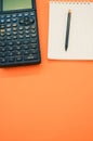 Top view closeup of a graphing calculator and a pen on a notepad isolated on an orange background