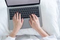 Top view closeup image of woman`s hands typing on laptop on the bed