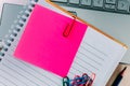 Top view closeup of a pink sticky note inside of a notebook, secured with a paper clip and a laptop