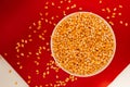 Top view closeup of a popcorn bowl with some corns spilled around it isolated on a red background
