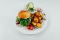 Top view closeup of roasted potatoes with tomato and radish next to a burger with arugula