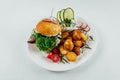 Top view closeup of roasted potatoes with tomato and radish next to a burger with arugula