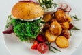 Top view closeup of roasted potatoes with tomato and radish next to a burger with arugula