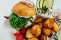 Top view closeup of roasted potatoes with tomato and radish next to a burger with arugula