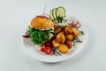 Top view closeup of roasted potatoes with tomato and radish next to a burger with arugula