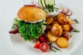 Top view closeup of roasted potatoes with tomato and radish next to a burger with arugula