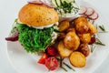 Top view closeup of roasted potatoes with tomato and radish next to a burger with arugula