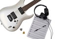 Top view of closeup of white electric guitar, two mediators, music paper for notes and guitar tabs, pen and headphones. Workspace