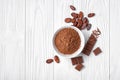 Top view of cocoa powder and beans with broken chocolate bar on white wooden background