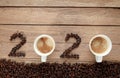 Top view of coffee beans and hot fresh coffee in a white cup with foam and text 2020 for Happy New Year Concept. on wooden table Royalty Free Stock Photo