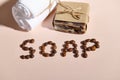 Top view of coffee beans laid out in SOAP word on pink background with natural soap bar - a body scrub and white towel.