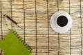 Top view of coffee beans with white cup, green notebook and pen on mat