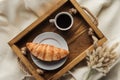 top view of coffee and croissant on tray with lagurus ovatus bouquet on beige cloth breakfast