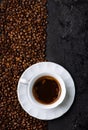Top view of coffee cup on coffee bean texture and black rustic background. Hot beverage on vintage dark table