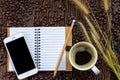 Top view of coffee cup, notebook, pencil, dry grass flower, coffee beans and smartphone with black blank screen on wooden table ba