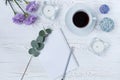 Top view of coffee mug, blank notepad, pencil, flowers and candles on white table. Flat lay