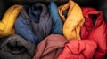 Top view of a collection of colorful winter jackets neatly folded and placed inside a dark storage bin, showcasing