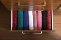 Top view of colored towels stored and organized in a wooden clothes guard drawer.