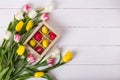 Top view of colorful easter eggs on a bed of straw in a long wooden box on a white wooden table and tulips Royalty Free Stock Photo