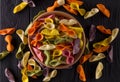 Top view of colorful farfalle pasta in bowl and scattered on black wooden table