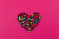 Top view of heart of multicolored beads on bright pink background.