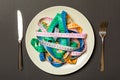 Top view of colorful measuring tapes on plate in the form of spaghetti with knife and fork on black background. Weight loss and Royalty Free Stock Photo