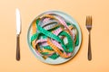 Top view of colorful measuring tapes on plate in the form of spaghetti with knife and fork on orange background. Weight loss and