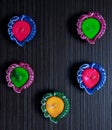 A top view of 5 colourful Diyas/Lamps arranged in diffrent ways