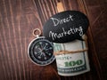 Top view compass, banknotes and coversation wooden board with text Direct Marketing