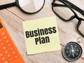 Top view compass,eye glasses,calculator and magnifying glass with text BUSINESS PLAN written on wooden background.