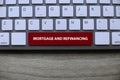 Top view of computer keyboard with red key written with Mortgage and Refinancing on wooden background